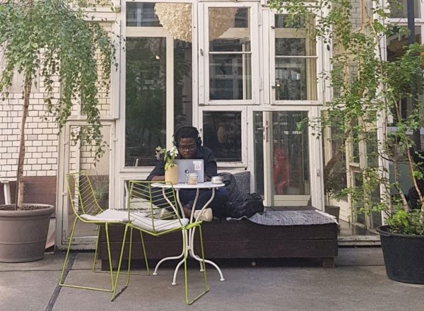 A person working on their laptop while sitting outdoors surrounded by large potted plants.