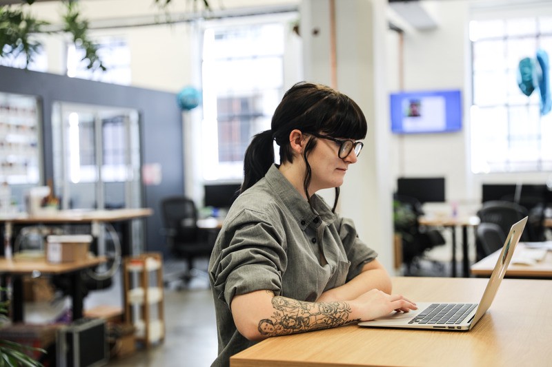 A person working on a laptop indoors while sitting at a desk at an office.