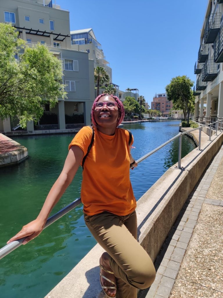 A person leaning on a railing outdoors next to a channel of water on a clear, sunny day.