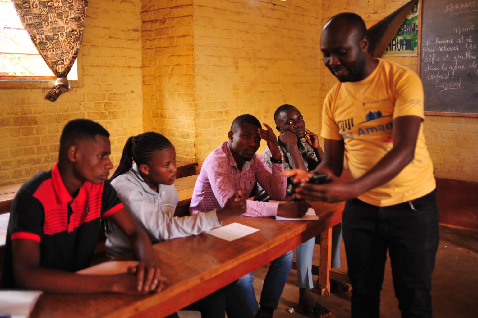 Several people sitting at desks in a classroom with an instructor speaking to them.