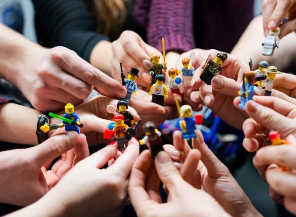 Several hands in a circle holding lego figures.